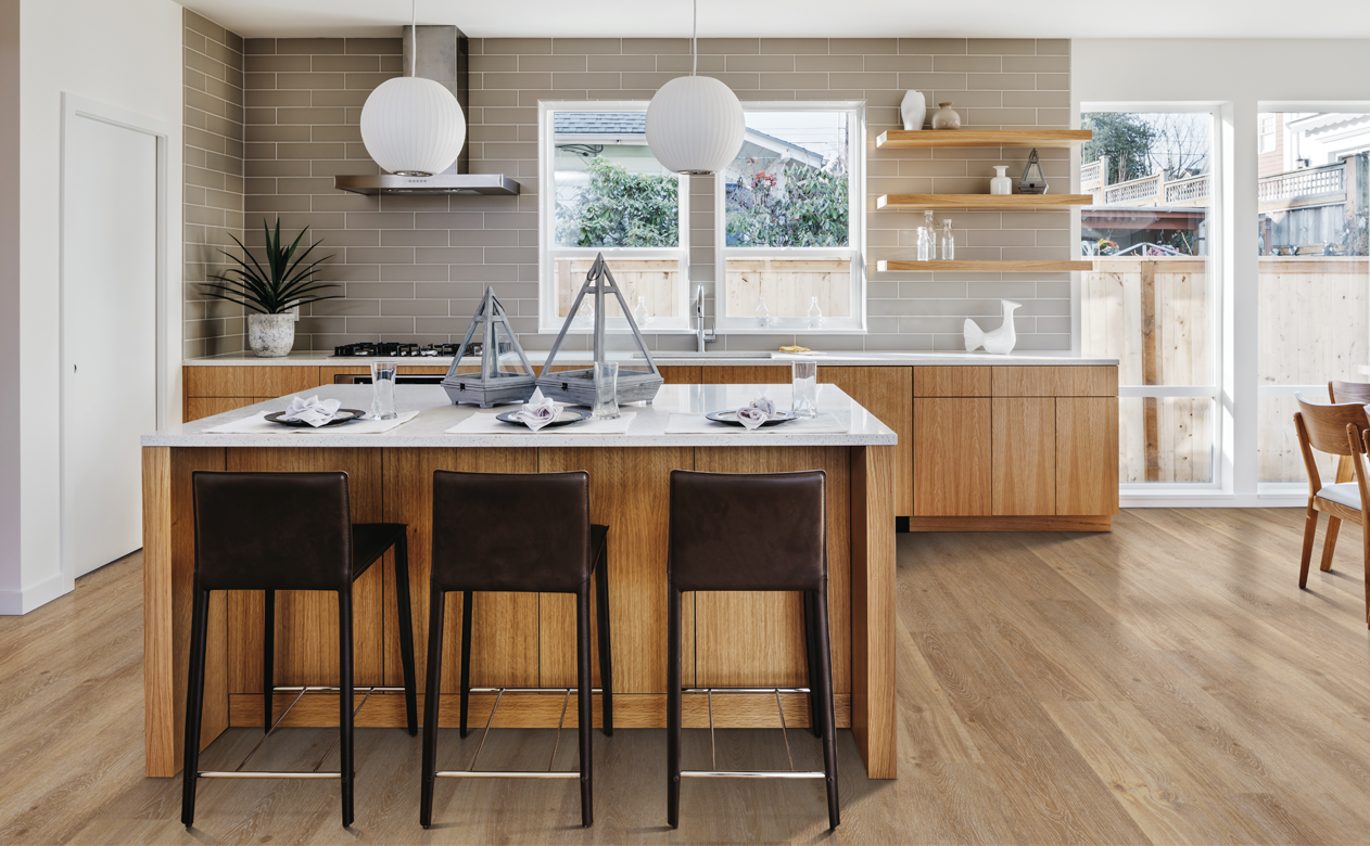 light brown subway tile backsplash in kitchen with white stone countertops and light wood modern cabinets